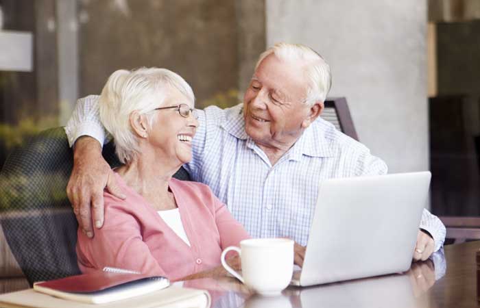 Older couple smiling at each other in front of a laptop.