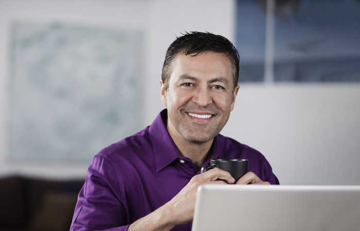Man holding a mug smiling in front of a laptop